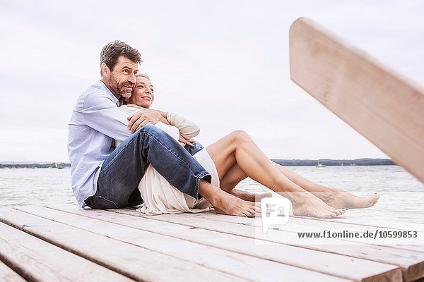 Erwachsenes Paar sitzend  umarmend  am Pier
