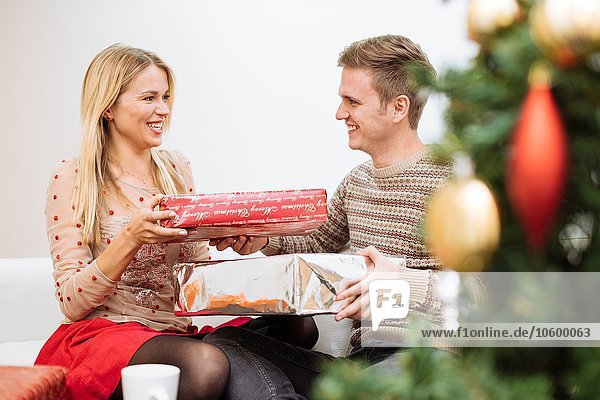 Junges Paar tauscht Weihnachtsgeschenke im Wohnzimmer aus
