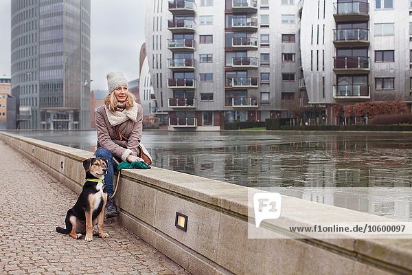 Mittlere erwachsene Frau und ihr Hund sitzen auf der Uferpromenade.