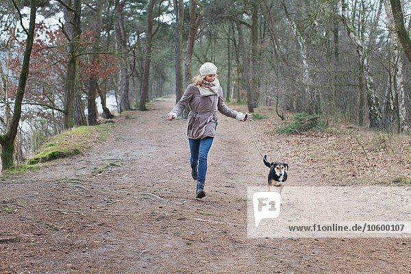 Mittlere erwachsene Frau  die mit ihrem Hund im Wald läuft.