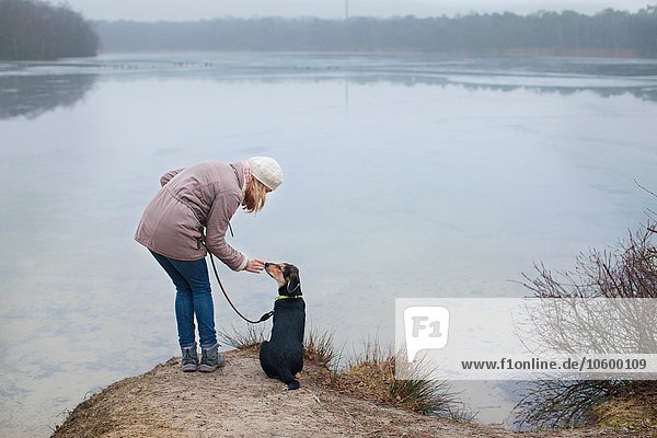 Mittlere erwachsene Frau  die ihren Hund am Flussufer streichelt.