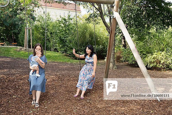Young woman with mother and baby daughter sitting on swings in park