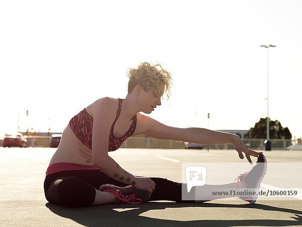 Junge Frau berührt ihre Zehen beim Training auf dem Parkplatz
