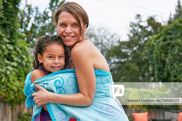 Mother and daughter wearing swimwear wrapped in towel looking at camera smiling