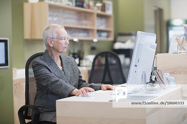 Senior female receptionist using desktop computer at hotel reception desk