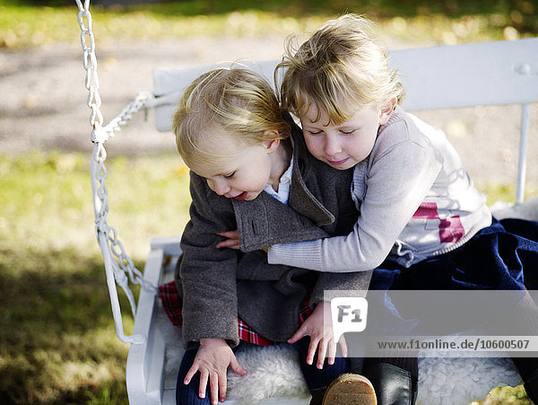 Two girls sitting on swing and playing