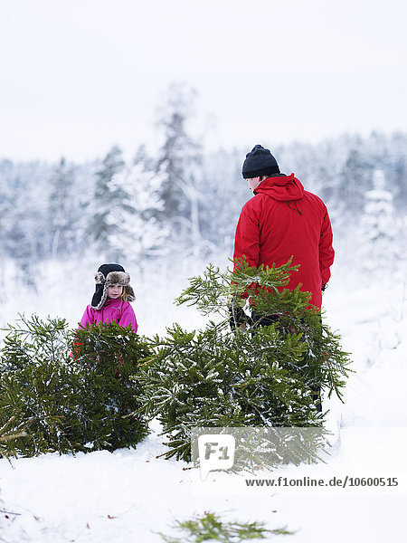 Vater und Tochter stehen neben einem kleinen Weihnachtsbaum im Schnee