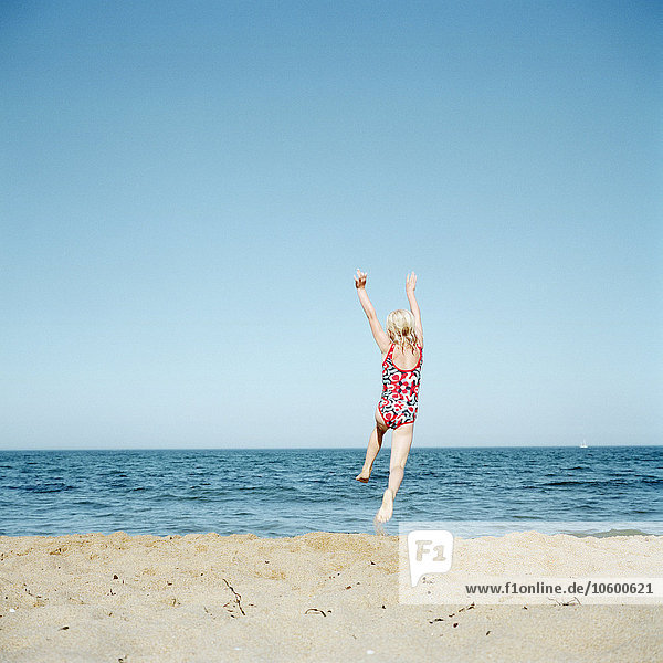 Mädchen springt am Strand  Rückansicht