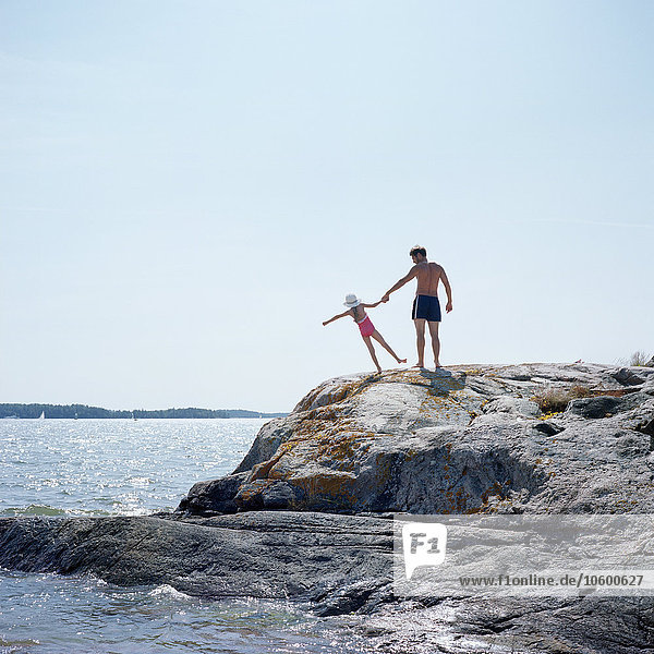 Vater und Tochter stehen auf einem Felsen am Meer