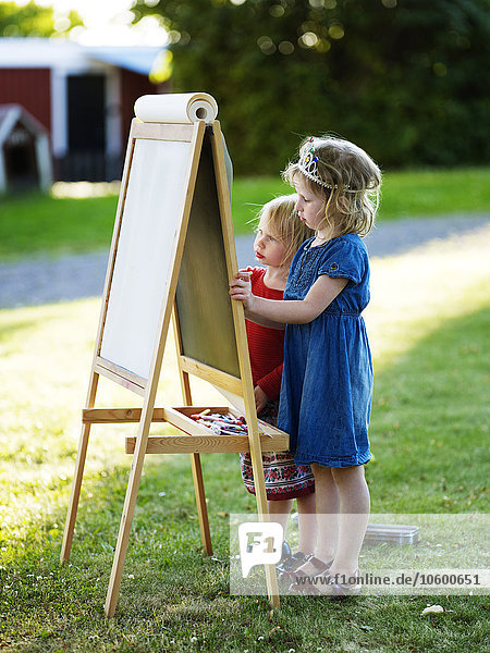 Two girls painting at easel on lawn