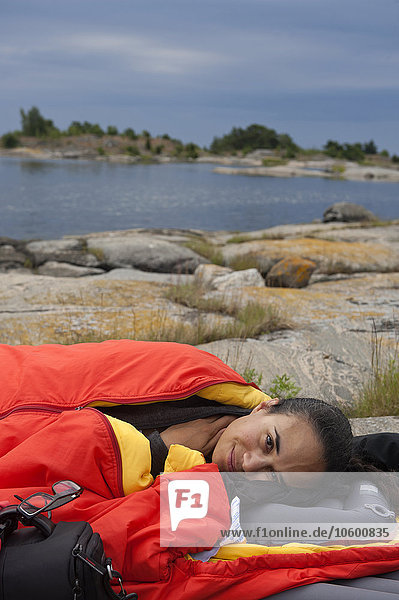 Frau im Schlafsack am Meeresufer liegend