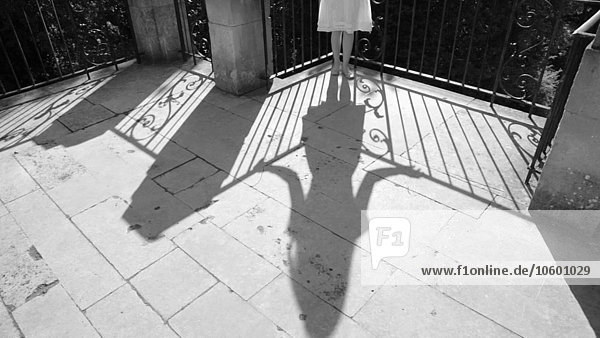 Schatten einer jungen erwachsenen Frau  die am Balkongeländer steht  Rock und Haare wehen im Wind