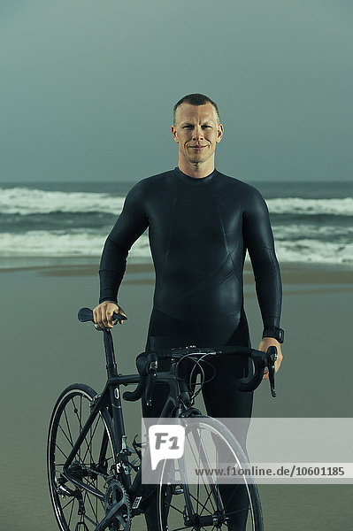 Man wearing wetsuit with bicycle on beach