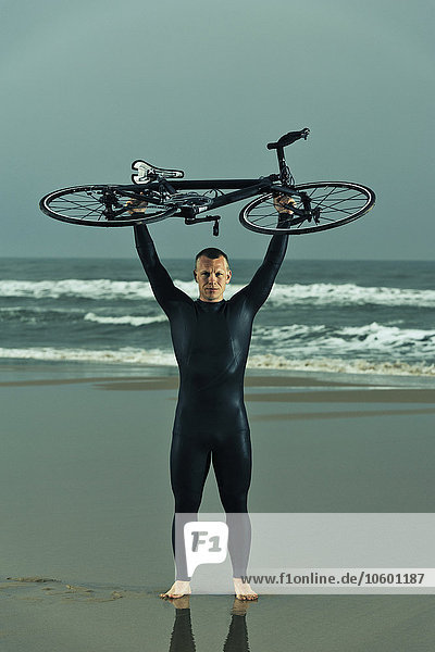 Man wearing wetsuit holding bicycle on beach