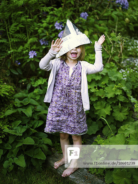 Lachendes Mädchen mit Papierhut im Garten