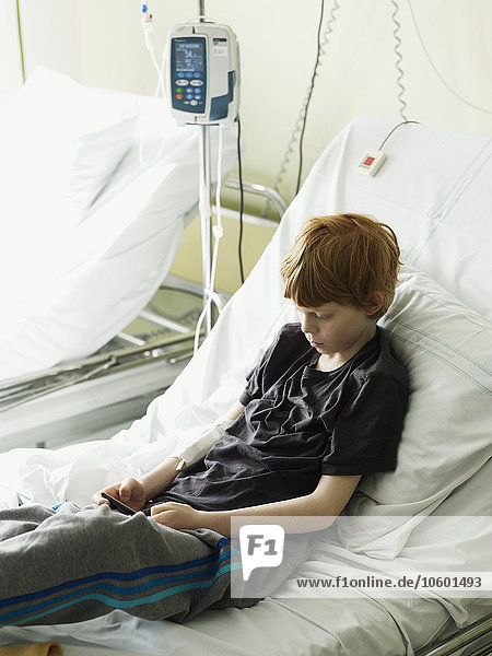Junge sitzt auf Krankenhausbett und schreibt SMS