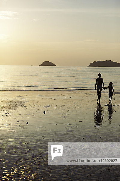 Mutter mit Sohn spazieren am Strand in der Abenddämmerung