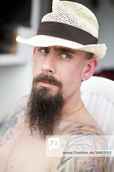 Mann mit Hut und Tattoos auf dem Arm