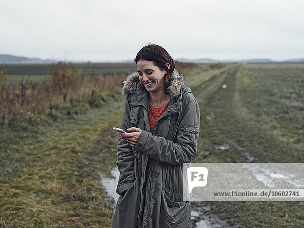 Smiling woman using cell phone on field road