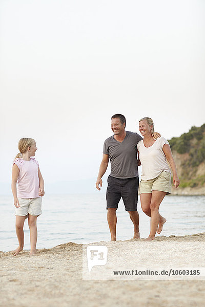 Eltern mit Tochter gehen am Strand spazieren