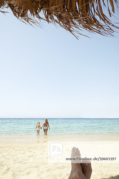 Mann entspannt sich am Strand  Frau mit Tochter im Hintergrund