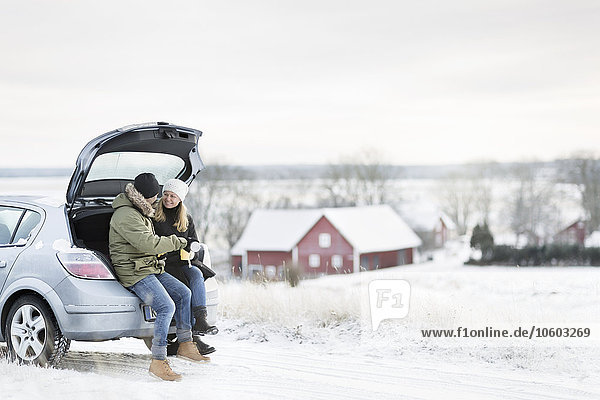 Smiling couple sitting in open boot
