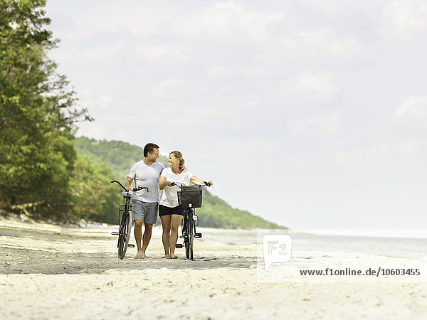 Couple with bicycles walking on beach