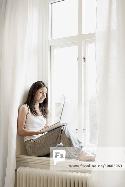 Frau auf der Fensterbank sitzend und mit Laptop