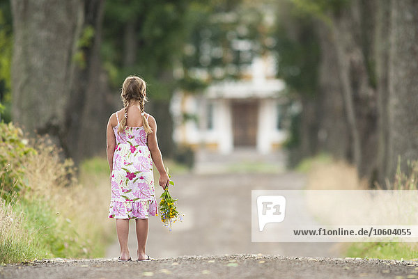 Mädchen mit Wildblumen auf der Landstraße stehend