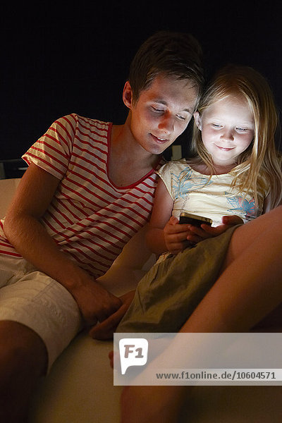 Bruder mit Schwester schaut nachts auf das Handy