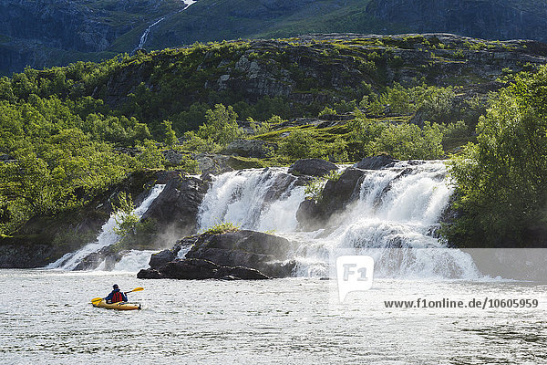 Mann fährt Kajak in der Nähe eines Wasserfalls