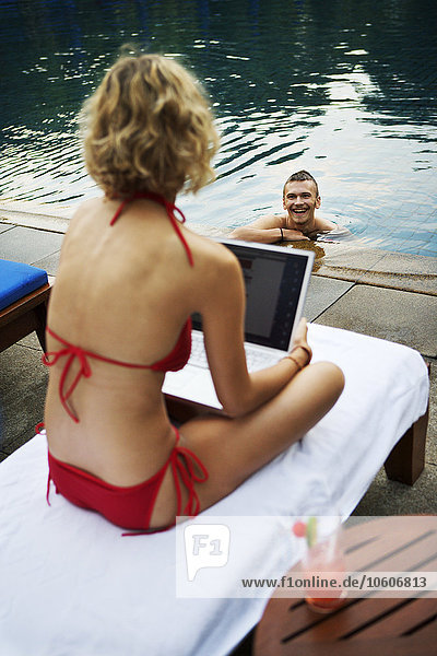 Eine skandinavische Frau mit einem Laptop an einem Swimmingpool  Thailand.