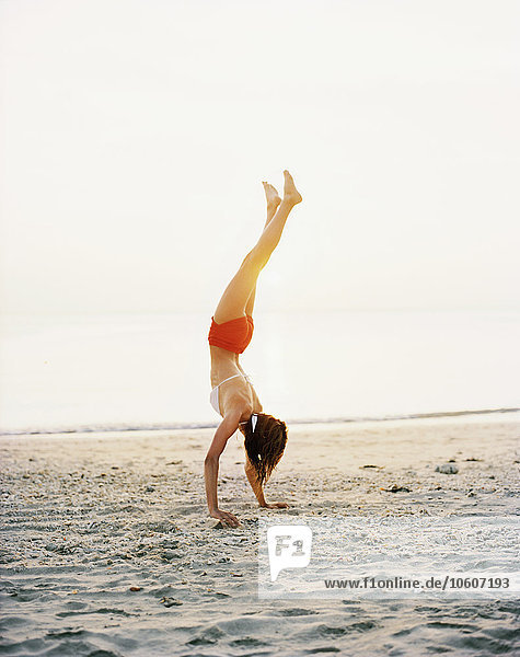 A Scandinavian woman doing a handstand on a beach.