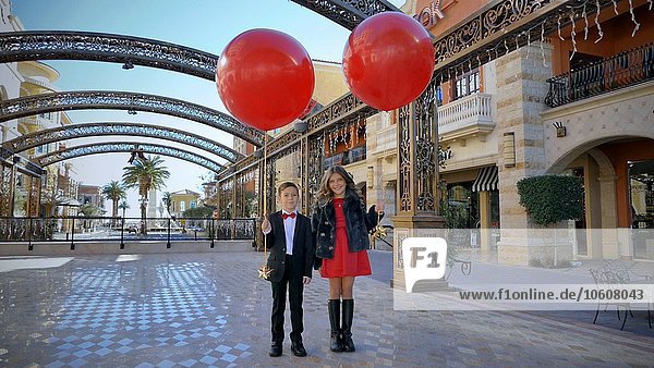 Junger Junge und Mädchen halten große rote Luftballons