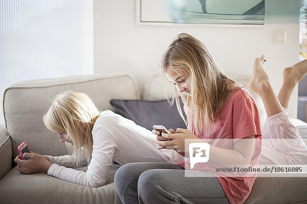 Teenage girls on sofa using cell phones