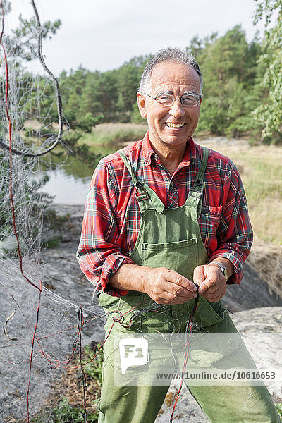 Lächelnder älterer Mann  der ein Fischernetz repariert
