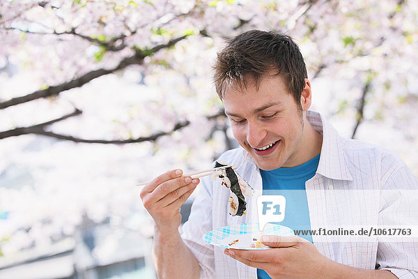Kaukasischer Mann isst Sushi mit Stäbchen während der Hanami-Saison