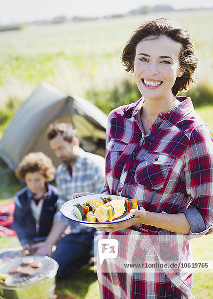 Portrait lächelnde Frau mit Gemüsespießen auf dem Campingplatz
