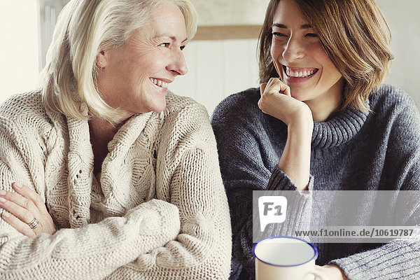 Lachende Mutter und Tochter in Pullovern beim Kaffeetrinken