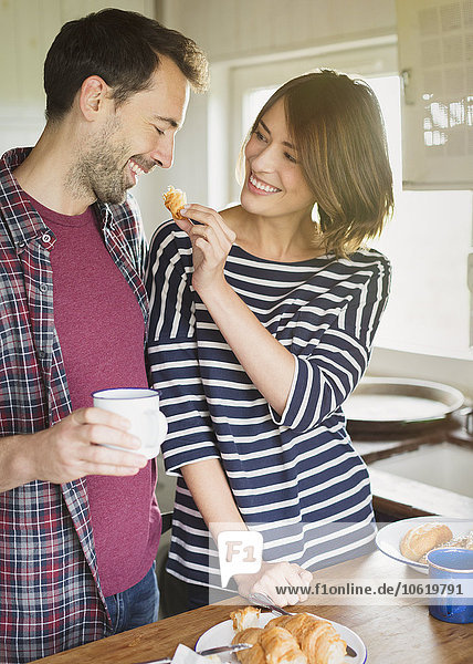 Girlfriend feeding boyfriend croissant in kitchen