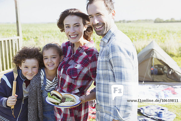 Portrait lächelnde Familie mit gegrillten Hamburgern auf dem sonnigen Campingplatz