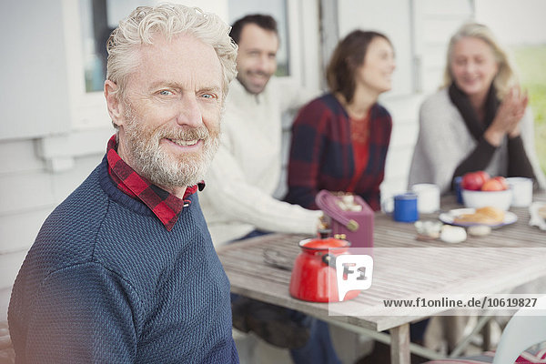 Portrait lächelnder älterer Mann beim Frühstück mit der Familie auf der Terrasse