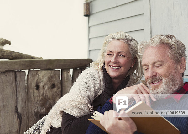 Lächelndes Seniorenpaar beim Lesen auf der Terrasse