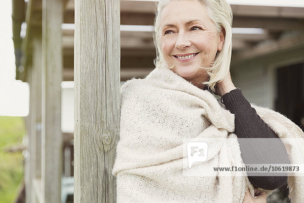 Lächelnde Seniorin mit Schal auf der Veranda