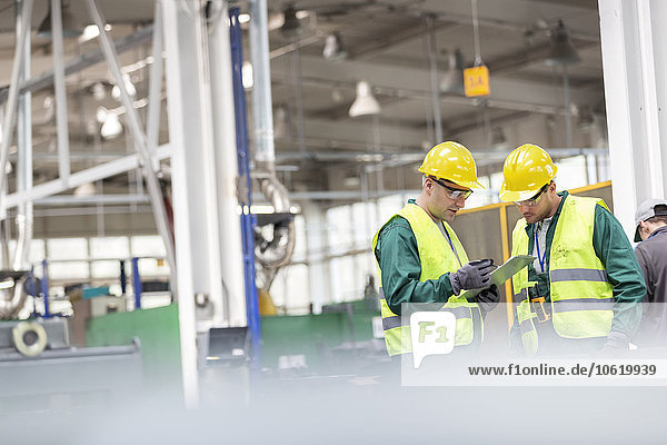 Arbeiter in schützender Arbeitskleidung im Gespräch mit der Zwischenablage in der Fabrik