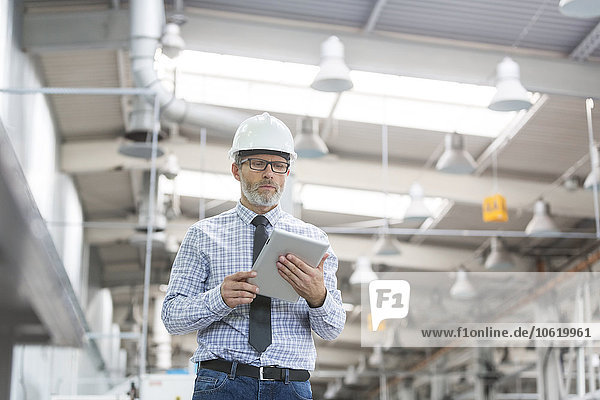 Engineer with hard-hat and digital tablet walking in factory