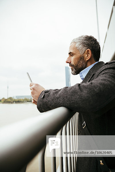 Österreich  Wien  Geschäftsmann auf der Reichsbrücke mit Blick auf sein Smartphone