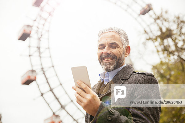 Österreich  Wien  Porträt eines lächelnden Geschäftsmannes mit Blick auf sein Smartphone im Prater