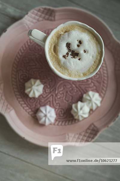 Tasse weißer Kaffee mit Schokoladenrasur und Meringues auf einem Teller