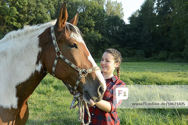 Junge Frau steht auf dem Feld und hält ihr Pferd.